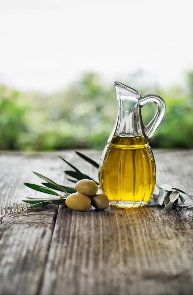 Brocca di vetro con olio extravergine e olive fresche sul tavolo
